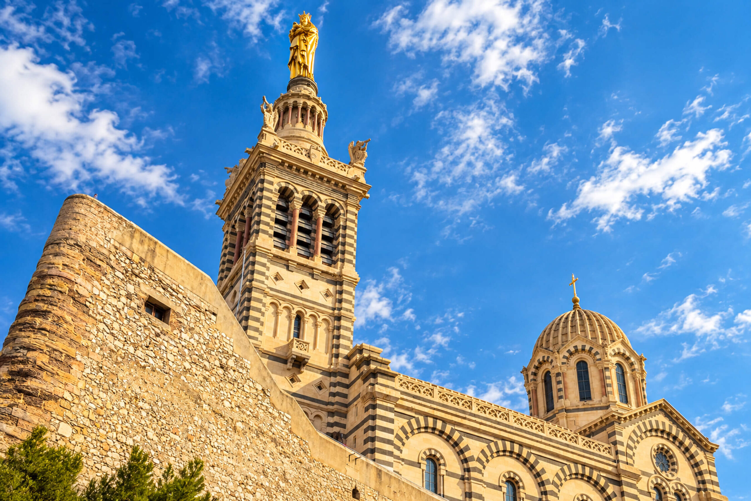Clocher de Notre-Dame de la Garde surmonté de la Bonne Mère dorée et coupole rayée, vus d’en bas